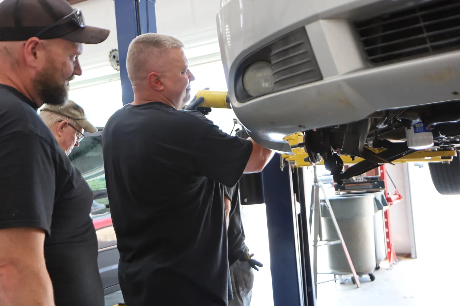 Volunteer mechanics working beneath a raised vehicle at Next Level Church